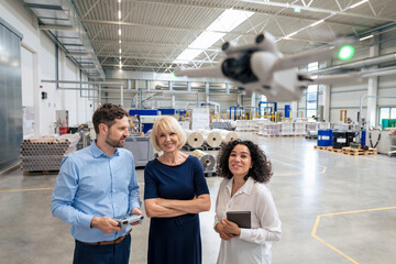 Smiling businesswoman holding tablet PC standing with colleagues analyzing flying drone in industry