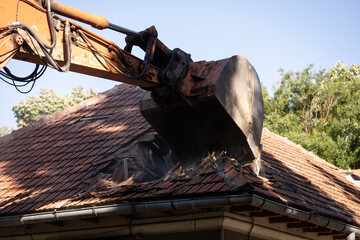 Heavy duty excavator demolishing an old house. Detail on the shingle roof demolish.