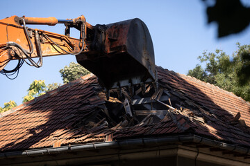 Heavy duty excavator demolishing an old house. Detail on the shingle roof demolish.