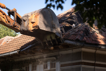 Heavy duty excavator demolishing an old house. Detail on the shingle roof demolish.