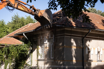 Heavy duty excavator demolishing an old house. Detail on the shingle roof demolish.