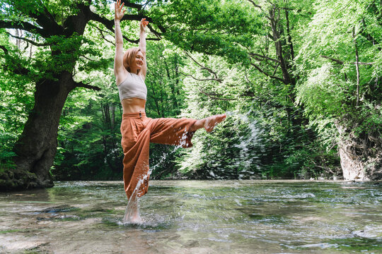 Woman enjoying a peaceful moment splashing water in a stream in a lush forest
