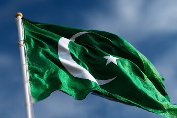 Waving Pakistan flag a green field with a white crescent and star against a blue sky