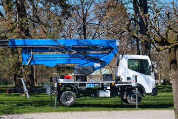 Industrial concrete pump truck featuring extended blue hydraulic boom arm stationed in peaceful park surroundings with mature trees and green lawn © JairoMZ