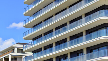 Exterior of a high modern multi-story apartment building - facade, windows and balconies. Modern glass balcony railings.