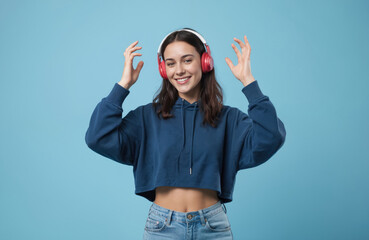 Cheerful young woman dances studio. She listens music headphones. Smiling, wearing blue hoody, jeans. Happy female enjoying song, smiling, fun and joy. Caucasian model, lifestyle.