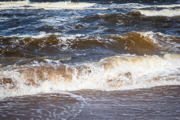 Brown Sea Waves Rolling onto Sandy Shore During Windy Weather