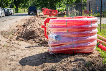 Red Corrugated Conduit Coils on Roadside at Construction Site for Underground Cable Installation