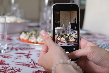 A girl takes a photo of a dish on her smartphone at a festive table. The concept of cooking, blogging, social networks, holiday, food