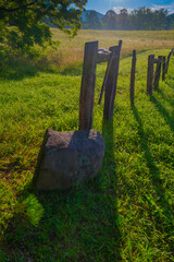 A fence in Cade's Cove lines a peaceful field and leads to trees and light fog and hearkens to a...