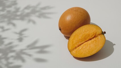 Two ripe mangoes, one whole and one halved, displayed against a backdrop of leaf shadows.