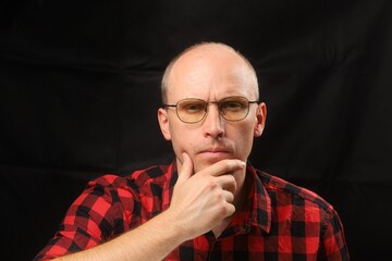 Thoughtful man in red checkered shirt poses against dark background