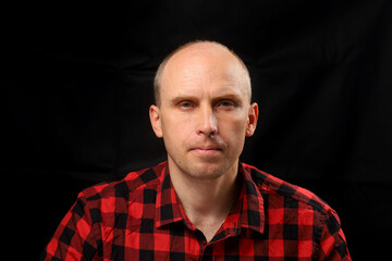 Man in red and black checkered shirt poses against dark backdrop
