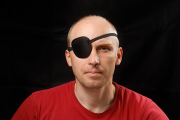 Man with an eye patch looks serious against a dark backdrop