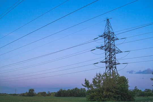 High voltage power transmission towers and power lines on green field at sunset. 