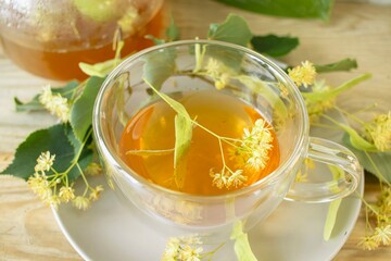 Linden tea in a glass cup with fresh linden flowers, on a wooden background. Medicinal herbal tea.