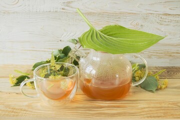 Linden tea in a glass cup with fresh linden flowers, on a wooden background. Medicinal herbal tea.