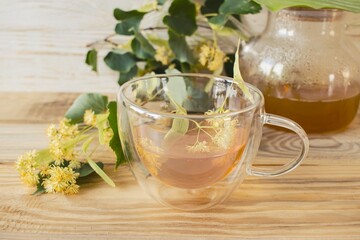 Linden tea in a glass cup with fresh linden flowers, on a wooden background. Medicinal herbal tea.