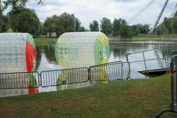 Water activity includes transparent inflatable balls ready for use near a calm lake in a park on a...