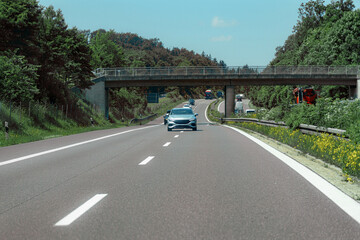 Clear highway view with a single car cruising under a bridge on a sunny day