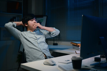 Tired businessman leaning back in office chair and yawning during late-night work session