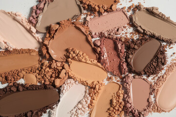 Colorful overlapping crushed and creamy makeup swatches in earthy tones arranged in a detailed flatlay on white background