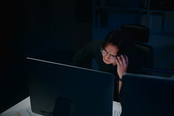 Businessman staying late at the office, with hand on head, feeling stressed and exhausted