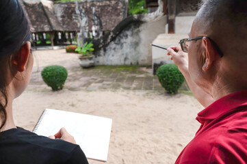 Male artist teacher teaching female art student how to draw historic Thai temple