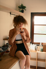 Relaxed woman wearing casual clothes, savoring a hot drink in cozy kitchen