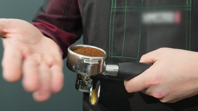 Man beats edge of palm on holder to flatten ground coffee beans. Work of professional in coffee shop. Tamping coffee mixture before brewing