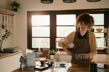 Young woman preparing a fresh cup of filter coffee in a bright kitchen
