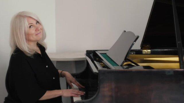 beautiful smiling caucasian woman pianist 45 years old plays the piano and looks at the camera, music teacher plays the piano in a music class