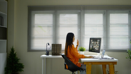 Young woman waving during a virtual meeting with colleagues, working remotely from home office
