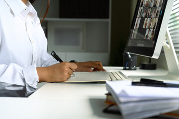 Close up of woman taking notes while attending a virtual meeting on her desktop computer