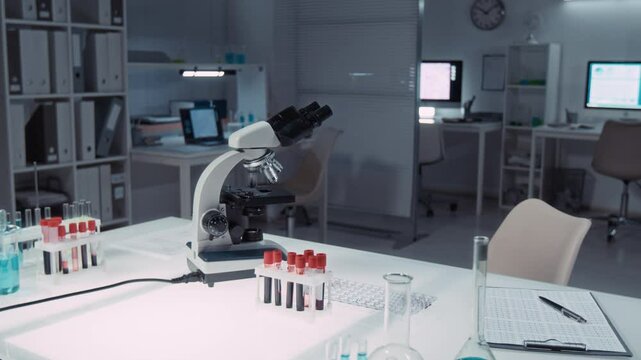 No people medium full panning shot of interior of diagnostic laboratory, with tubes of blood next to microscope and data report sheet, vials with reagents at bioengineering research company