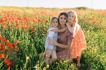 Happy mother with two daughters enjoying picnic in blooming poppy field. Family love concept.