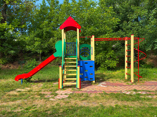 Bright and colorful children's playground in a park surrounded by green trees. The play structure...