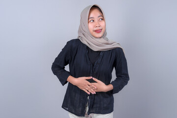 Portrait of a cheerful young Asian Muslim woman wearing hijab and casual outfit, smiling while...