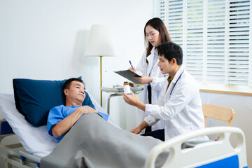 Obraz premium Doctor and nurse consult senior patient in hospital bed, discussing medicine & treatment. Caring medical team supports