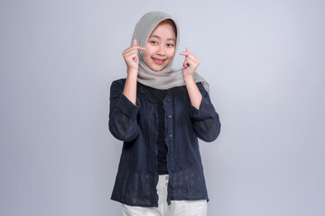 Portrait of a cheerful young Indonesian Muslim woman wearing a grey hijab and black blouse, smiling...