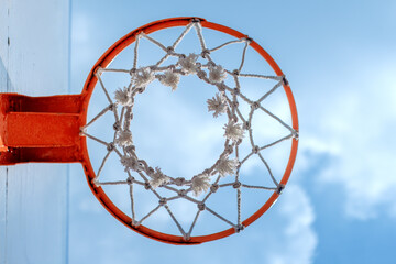 Close-up view of a basketball hoop with a white net, framed against a clear blue sky. The orange...