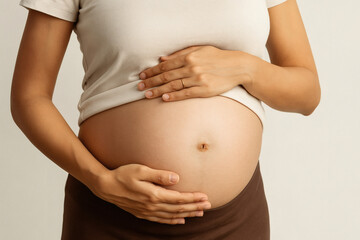 A pregnant woman gently places her hands on her belly