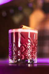 A stylish cocktail served in a crystal glass under vibrant pink and purple bar lights.
