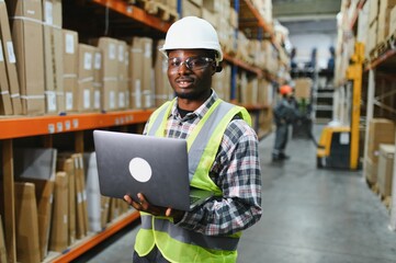 African american Warehouseman checking delivery, stock in warehouse on laptop. Warehouse manager...