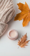 Cream jar, autumn leaves, cozy knitwear on white background