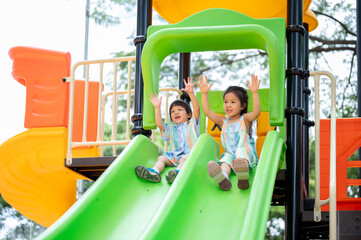 Asian girl and boy siblings happily playing on a colorful climbing slides in the park's playground.