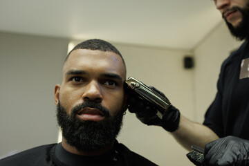 Barber trimming head of african american man in salon