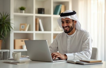 Happy arab man using laptop. Smiling muslim businessman at desk. Young male wearing traditional clothes works in home office. Digital device online, remote work, business concept.