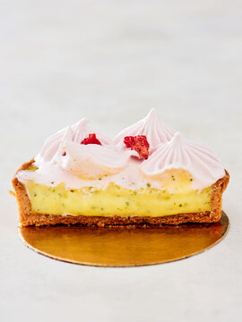 This dessert features a buttery pastry shell filled with rich custard, topped with light pink frosting and garnished with dried raspberries, inviting indulgence