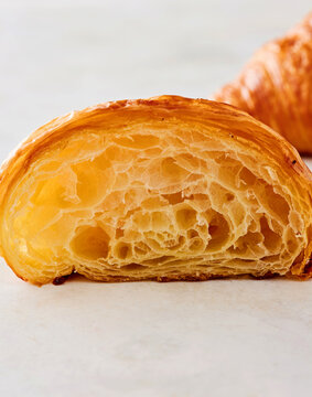 A freshly baked croissant sits on a marble surface, sliced in half to expose its flaky layers. The golden crust contrasts with the soft, airy interior, inviting a delicious experience